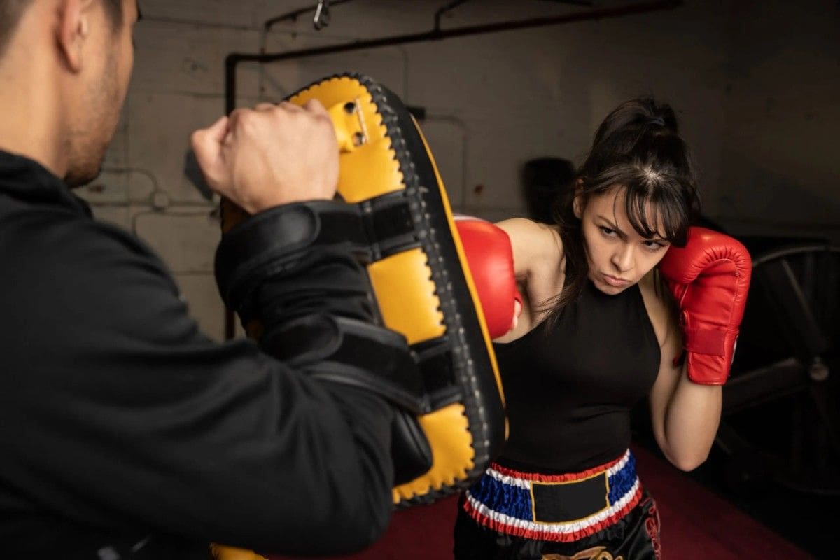Female fighter working pad drills with instructor during high-intensity boxing workout.